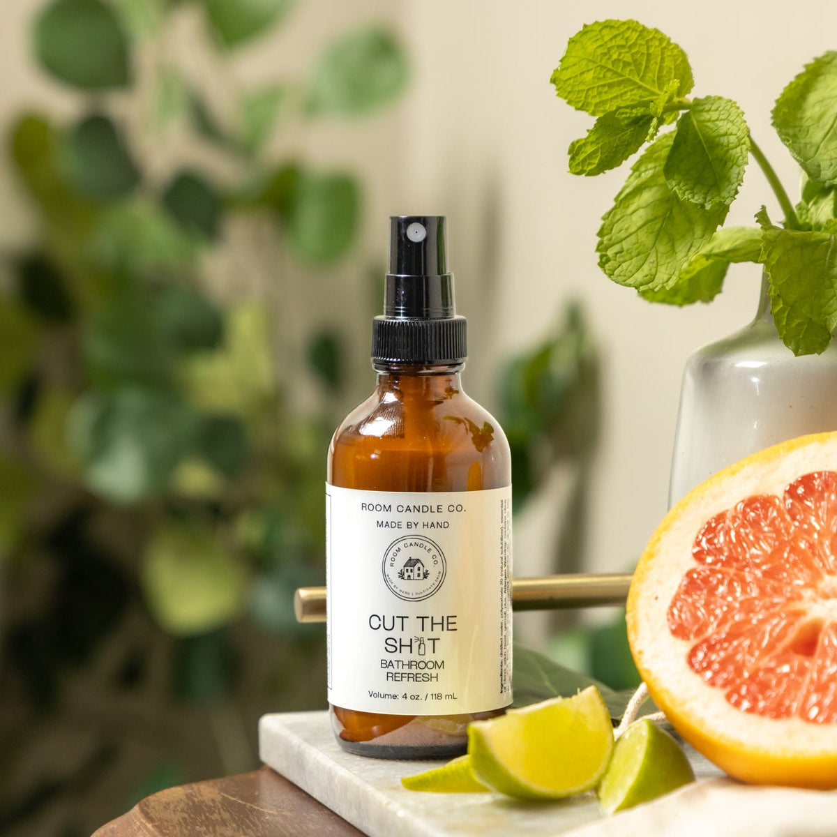 Room Candle Co.’s Cut the Sh*t bathroom refresh spray displayed on a counter with fresh grapefruit, mint leaves, and lime.