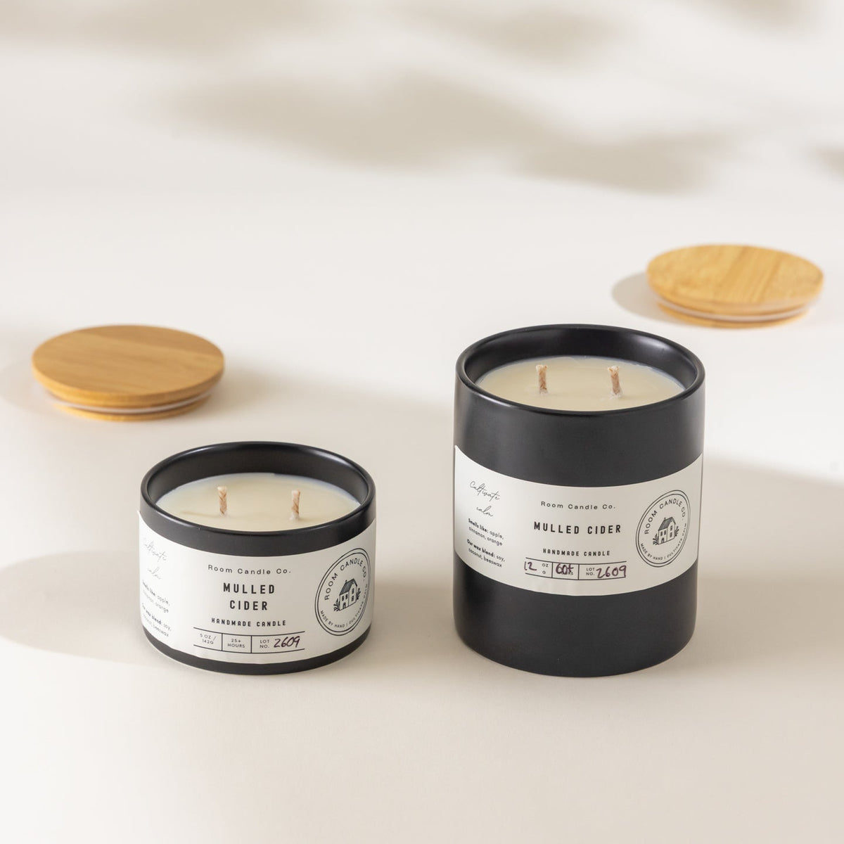 Two Mulled Cider candles by Room Candle Co. in 5 oz and 12 oz sizes, displayed in black ceramic vessels against a plain background.