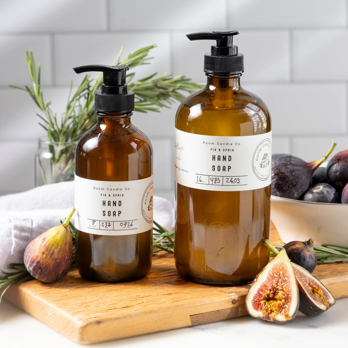 Two sizes of Fig and Sprig Liquid Hand Soap by Room Candle Co. in glass bottles with pump dispensers. Figs and rosemary.