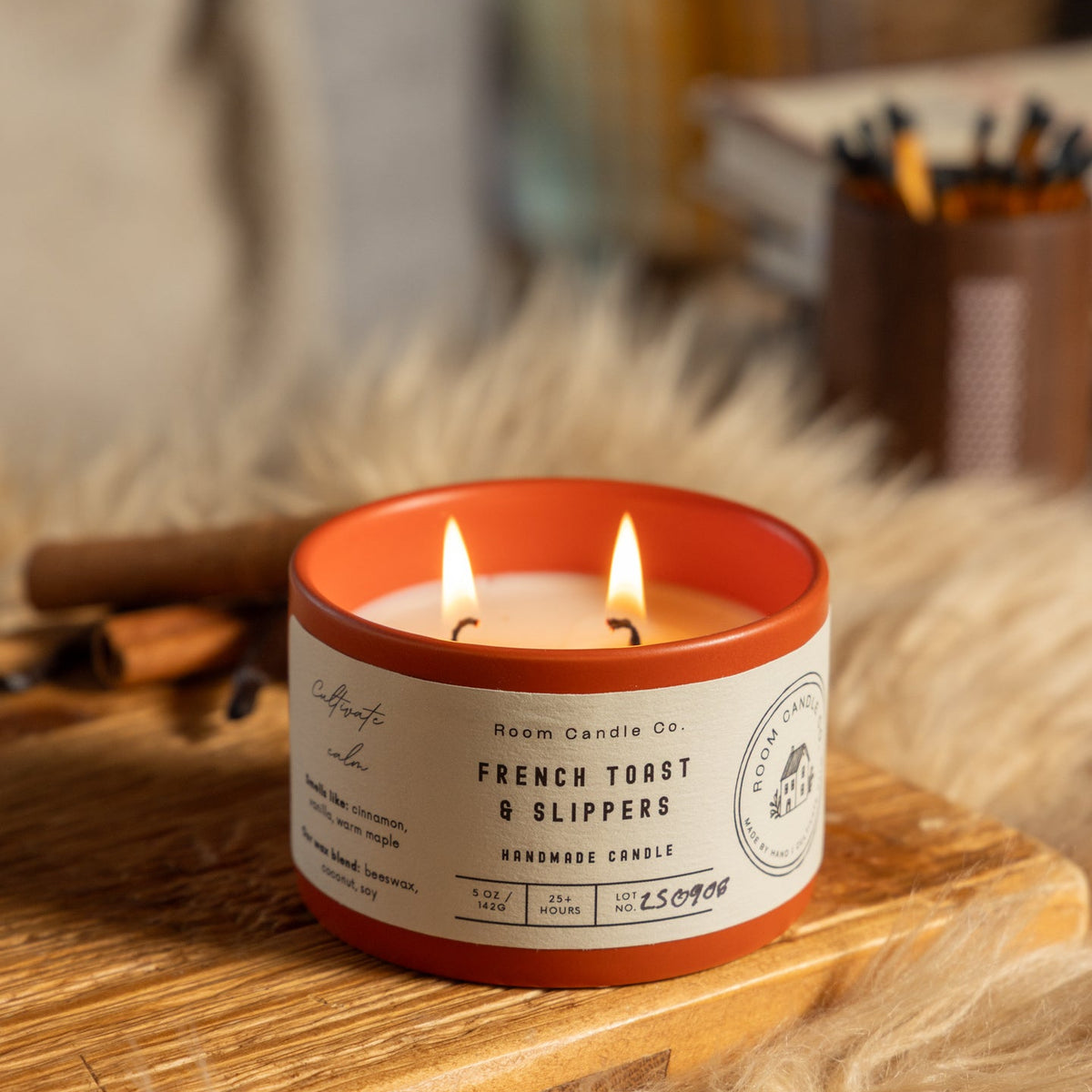 Lit 5 oz French Toast & Slippers candle by Room Candle Co. in a burnt sienna ceramic vessel, styled in a cozy setting with cinnamon sticks.