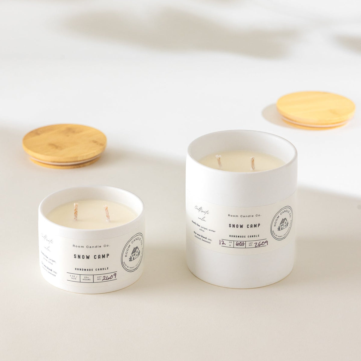Two Snow Camp candles by Room Candle Co. in 5 oz and 12 oz sizes, displayed in white ceramic vessels against a plain background.