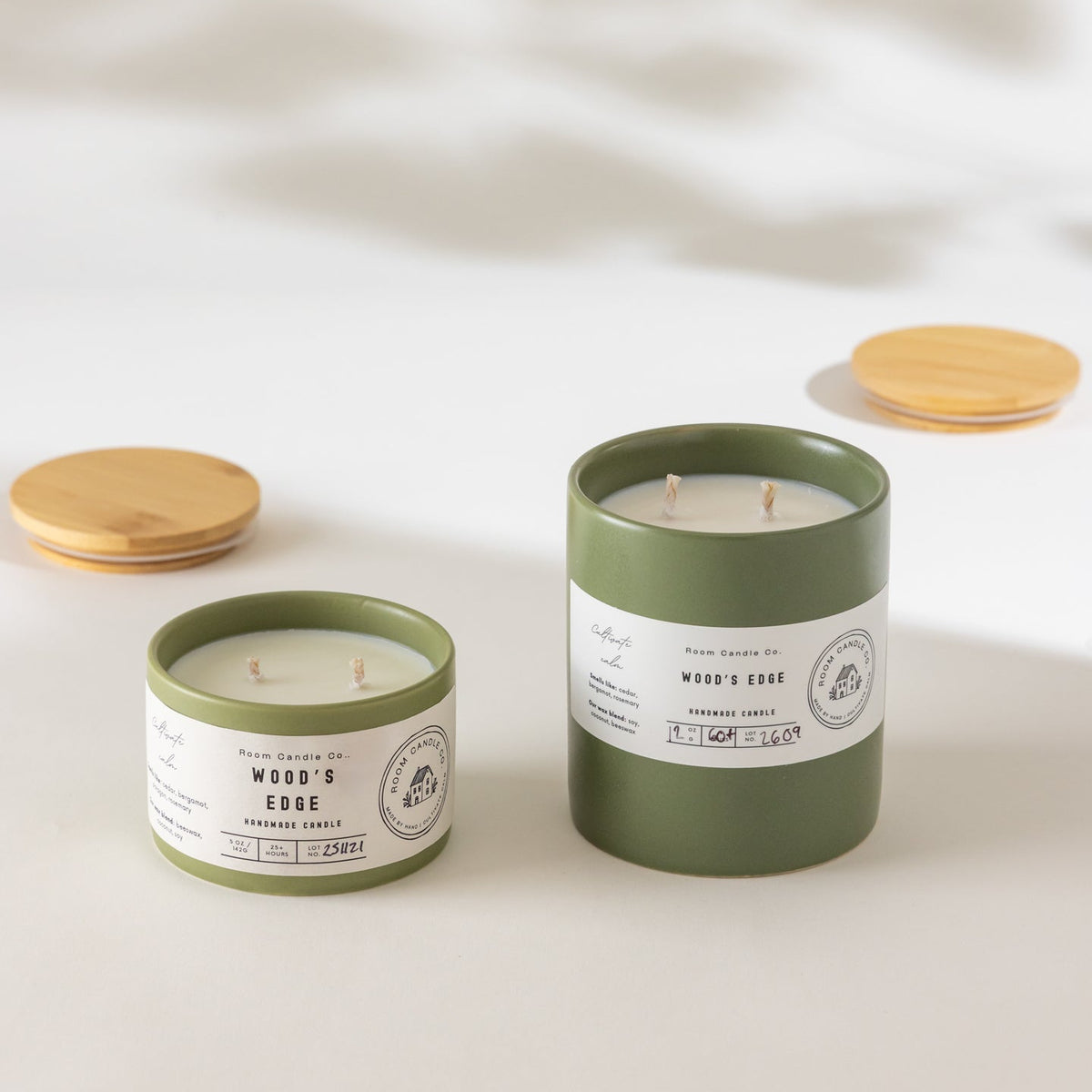 Two Wood’s Edge candles by Room Candle Co. in 5 oz and 12 oz sizes, displayed in green ceramic vessels against a plain background.